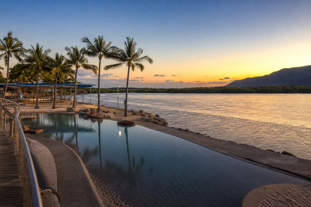 The free public swimming lagoon on the Cairns Esplanade waterfront with palm trees and the Coral Sea in the background